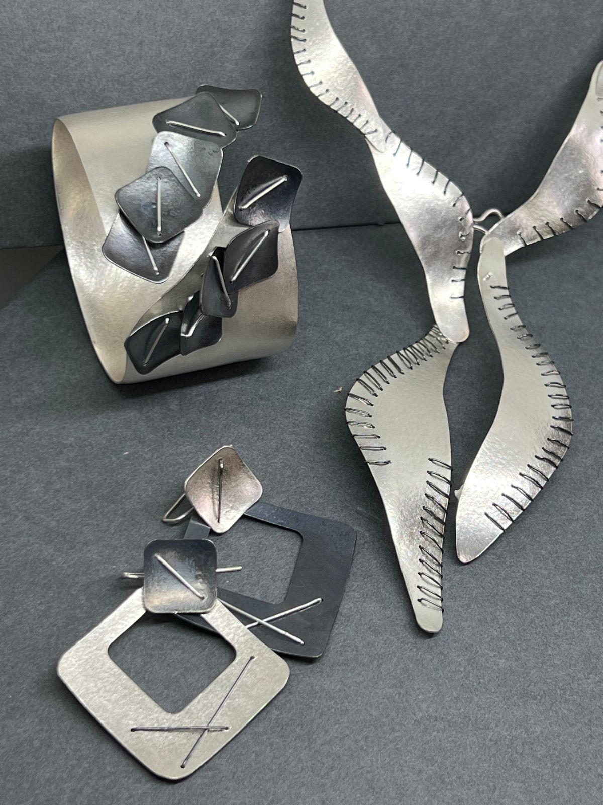 Suzanne Schwartz Jewelry collection featuring stitched silver cuff, 22k gold ring, and rutilated quartz leaf pendant
