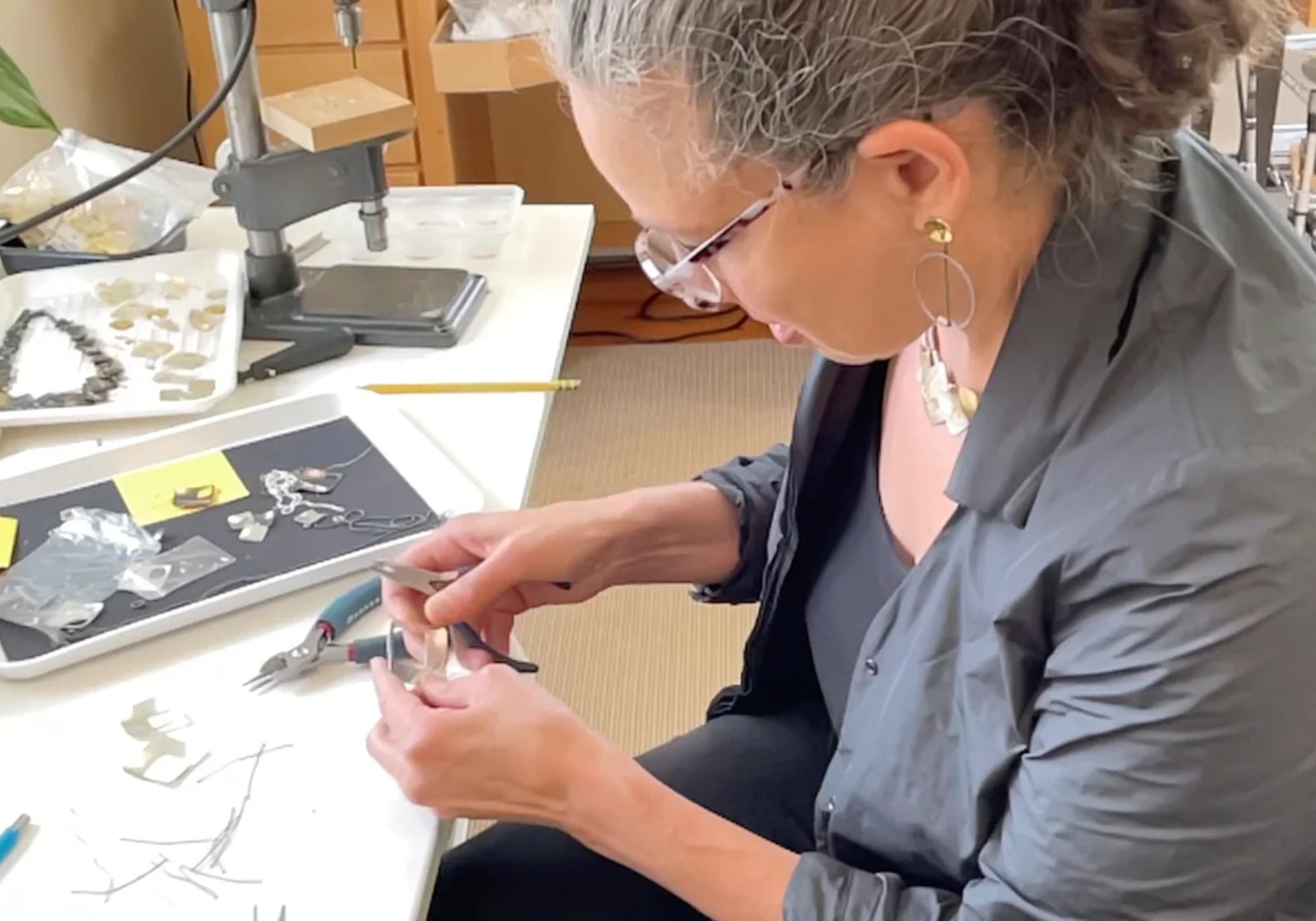 Suzanne Schwartz assembling handmade stitched metal jewelry with pliers at her New York studio